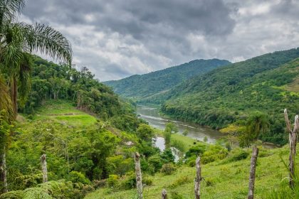 Rio sinuoso atravessando um vale coberto por vegetação, sob céu nublado.