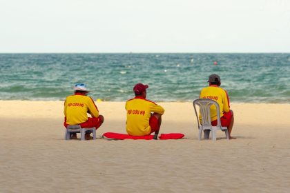 Três guarda-vidas uniformizados observam o mar sentados na areia da praia.